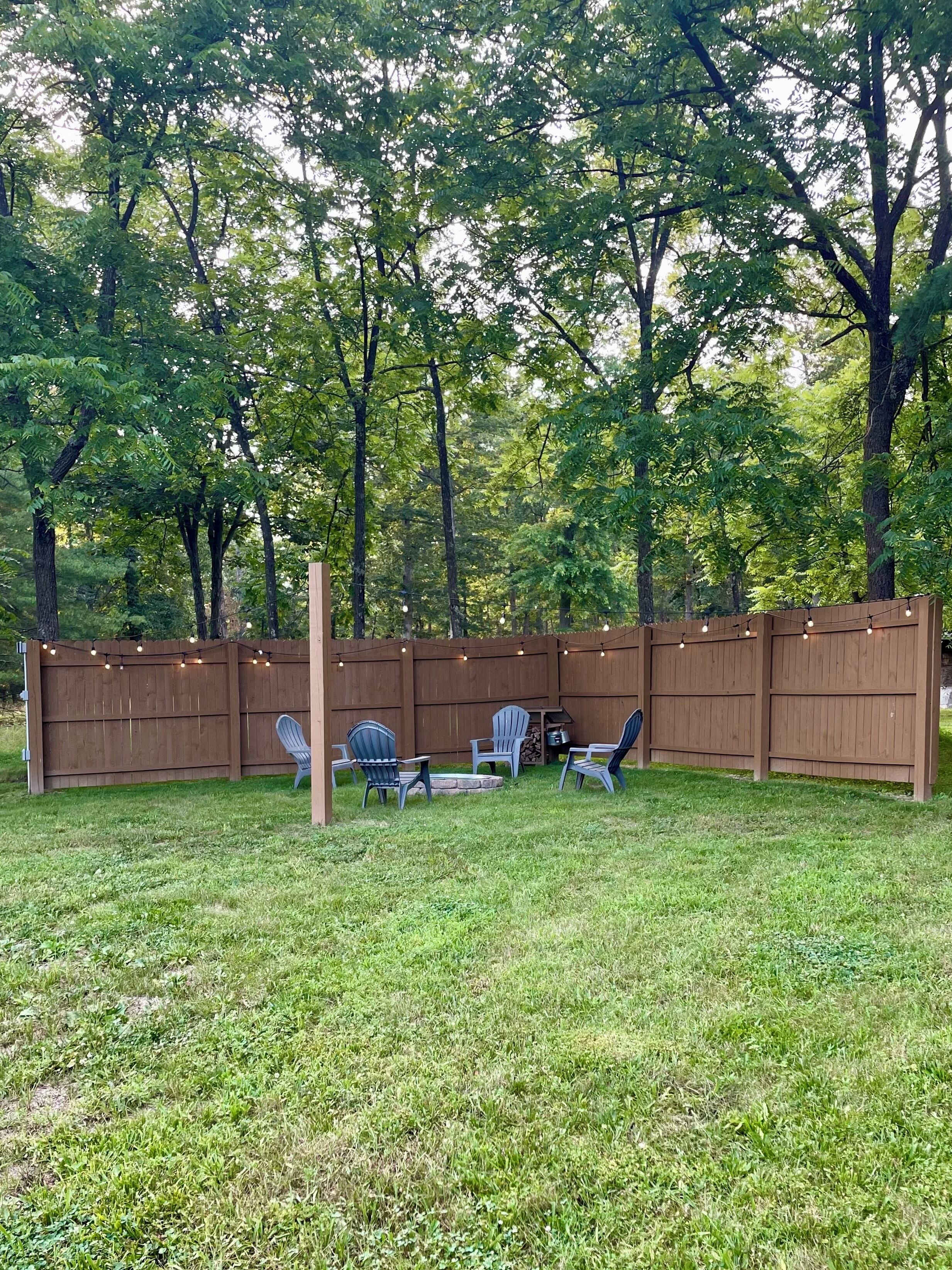 Un jardin avec une clôture en bois, des guirlandes lumineuses et deux fauteuils Adirondack.