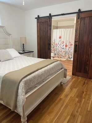 A bedroom with a bed, a nightstand, a lamp, and a view through a door with a floral curtain. - Oldtown Guesthouse (Oldtown)