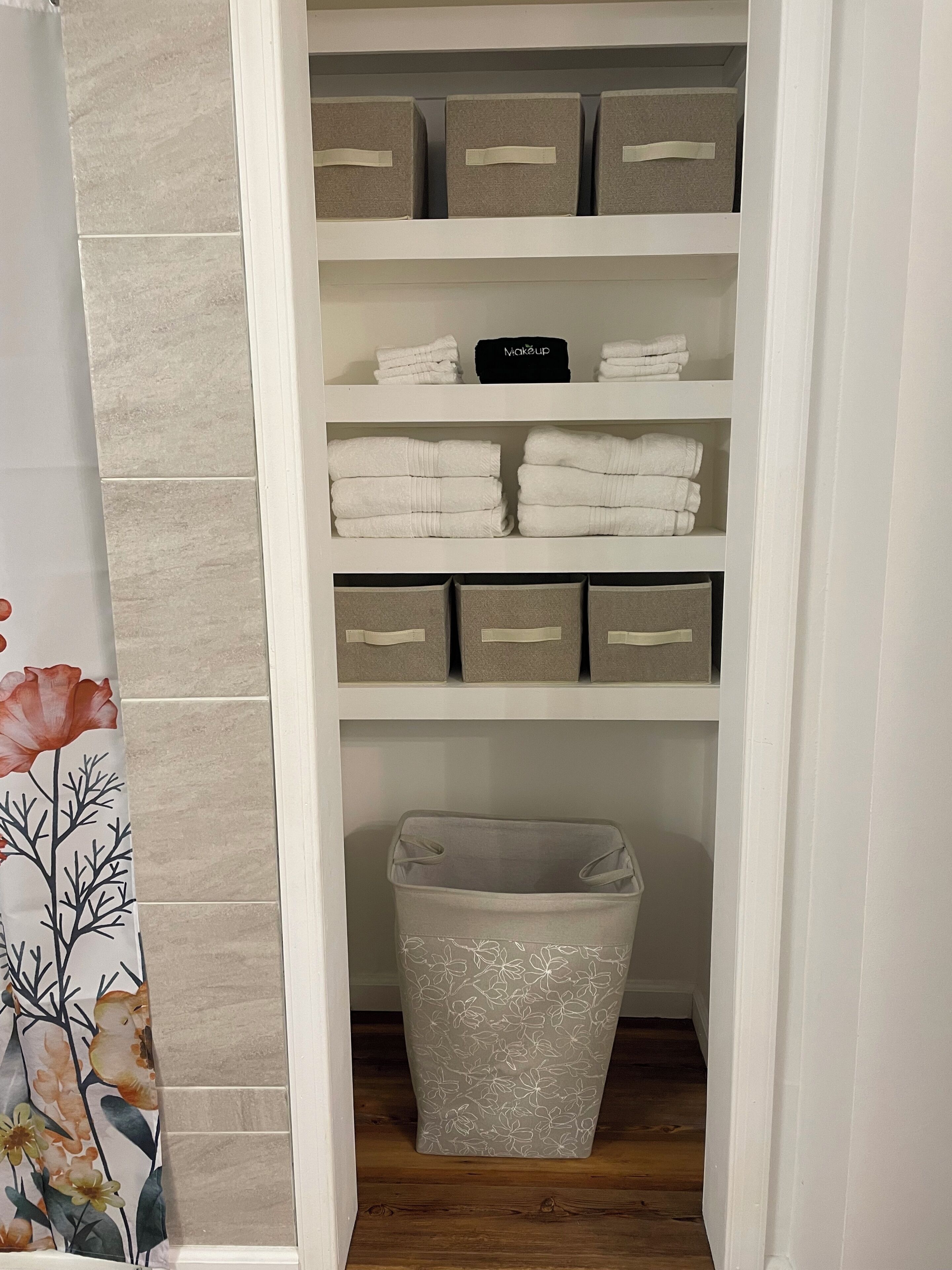 Un placard de rangement avec des étagères contenant des serviettes pliées et des boîtes de rangement.