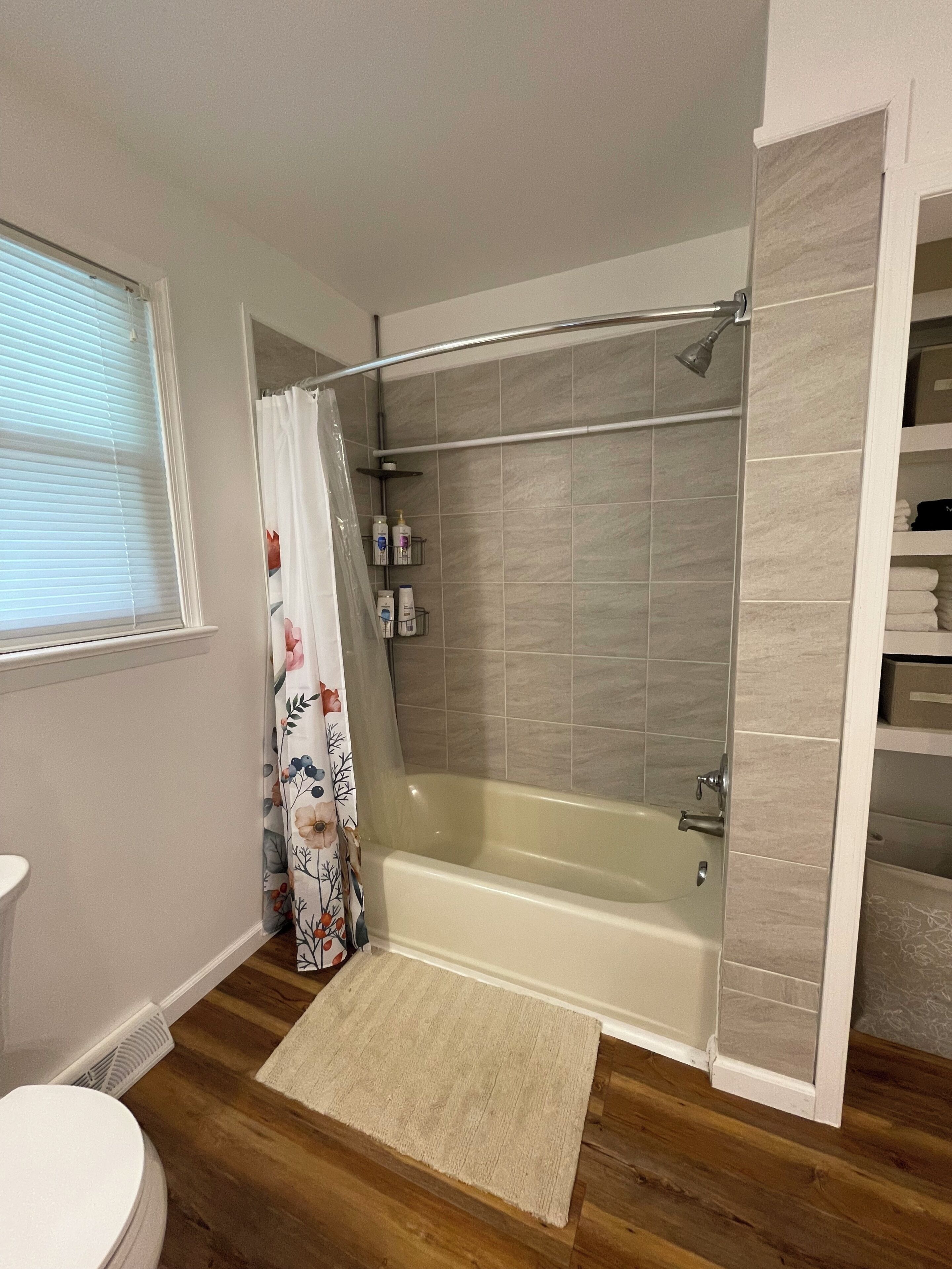 A bathroom with a bathtub, shower, toilet, and a window with blinds.