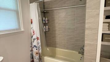 A bathroom with a bathtub, shower, toilet, and a window with blinds.