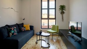 Un salon moderne avec un canapé foncé, une petite table ronde, un fauteuil vert, une grande fenêtre et un téléviseur à écran plat.