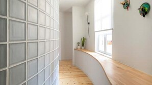 Un intérieur moderne avec un banc en bois aux lignes courbes, un mur blanc orné d’un motif quadrillé et une fenêtre laissant entrer la lumière naturelle.