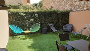 Eine kleine Terrasse im Freien mit Kunstgrashallett, verschiedenen Sitzmöglichkeiten und einer Heckenwand.
