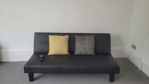 A black sofa with two cushions, a remote control, and three wall-mounted mirrors. - Beautiful 1-bed Apartment in Ramsgate (Ramsgate)