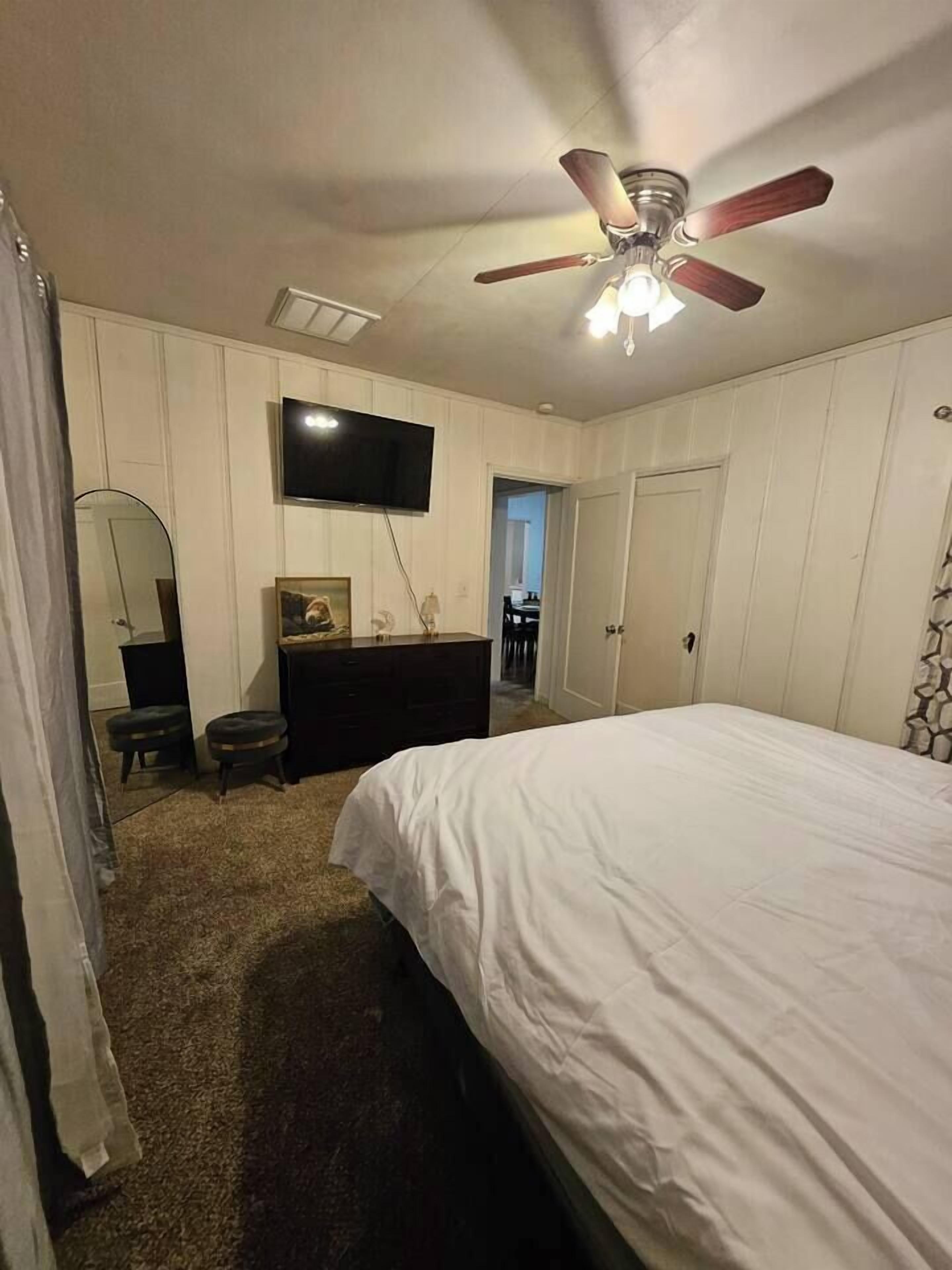 A bedroom with a bed, a ceiling fan, a TV, a dresser, and a mirror.