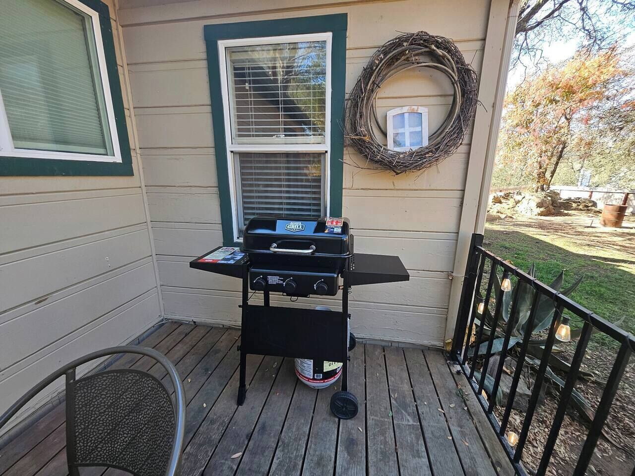 A barbecue grill on a wooden deck with a window and a wreath on the wall.