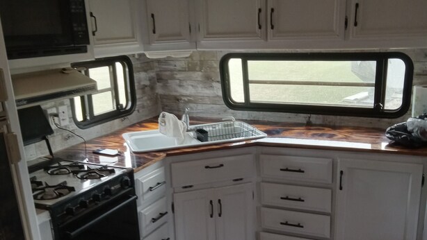 A compact kitchen with white cabinets, a stove, a microwave, and a window. - Relax and enjoy nature at the spacious North branch get away. 39 acres available (Hesperia)