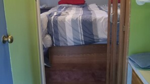 A narrow hallway leading to a bedroom with a bed, a red pillow, and a wooden door. - Relax and enjoy nature at the spacious North branch get away. 39 acres available (Hesperia)