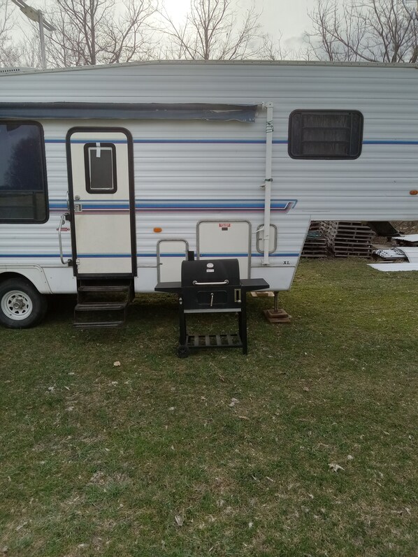 Un véhicule récréatif doté d’une porte coulissante, d’un petit espace clos équipé d’un barbecue et d’une rampe menant à la porte.