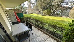 Un balcon avec une table et des chaises, un espace extérieur aménagé et abrité, et un jardin bien entretenu avec des haies et des arbres.