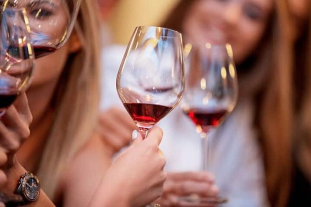 Primer plano de una copa de vino con líquido rojo, sostenida por una persona que lleva un reloj.