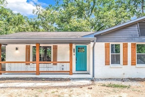A two-story building with a porch, a teal door, and wooden shutters.