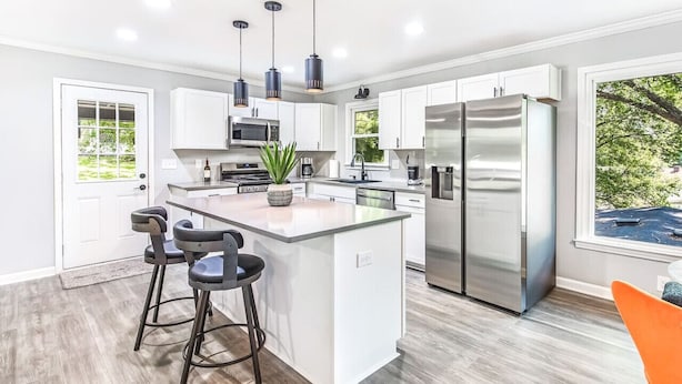 A modern kitchen with a central island, stainless steel appliances, pendant lighting, and a view of the outdoors.