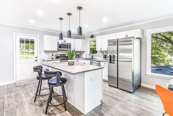 A modern kitchen with a central island, stainless steel appliances, pendant lighting, and a view of the outdoors.