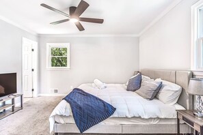 A bedroom with a bed, a ceiling fan, a TV, and a window with a view of greenery.