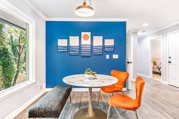 Ein modernes Zimmer mit blauer Akzentwand, einem runden Tisch mit Pflanze und zwei orangefarbenen Stühlen.