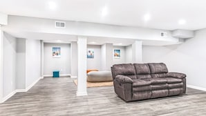 A spacious room with a grey leather sofa, a bean bag, and a small blue trash bin.