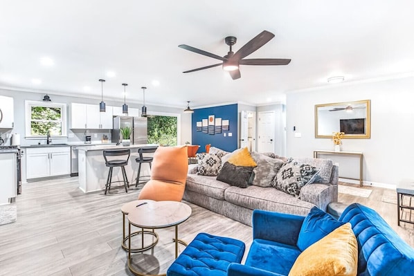 A modern living space with a kitchen, dining area, and a large sofa with multiple cushions.
