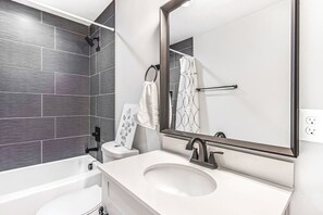 A modern bathroom with a white sink, a large mirror, a shower, and dark gray tiles.