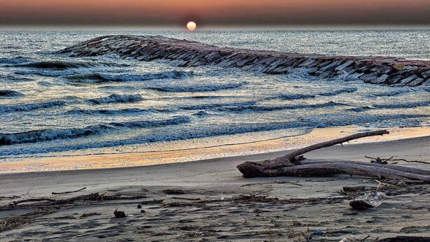 A beach with waves, a sunset, and driftwood. - Holiday apartment with balcony and air conditioning (Rosolina Mare)
