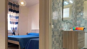 A bedroom with two beds, a bathroom with a tiled wall, and a wooden cabinet. - Holiday apartment with balcony and air conditioning (Rosolina Mare)
