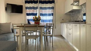 A modern kitchen with white cabinets, a built-in stove, and a window with striped curtains. - Holiday apartment with balcony and air conditioning (Rosolina Mare)