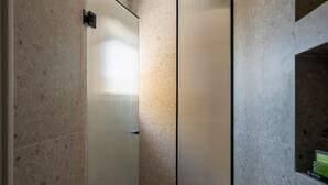 Een moderne badkamer met een glazen douchecabine, een zichtbaar bedieningspaneel voor de douche en een klein raam met uitzicht op groen.