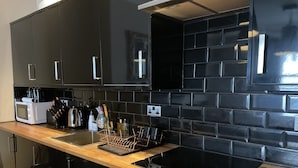 A modern kitchen with black cabinets, a wooden countertop, a built-in stove, and a microwave. - Brighton Beach Stylish 1 Bed Apartment (Brighton)
