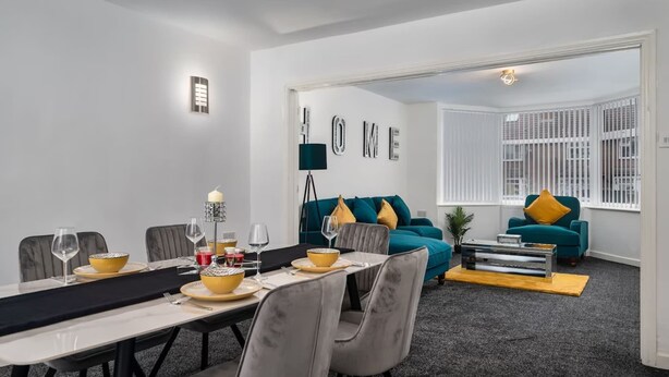 Un soggiorno moderno con divani color acquamarina, un'area pranzo con un tavolo lungo e un cartello con la scritta 'HOME'.