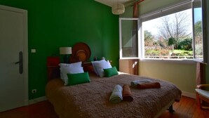 A bedroom with a large bed, green walls, a window with a view of trees, and a wooden floor.