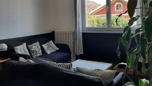 A living room with a dark blue sofa, a white coffee table, and a large window with a view of a red house.