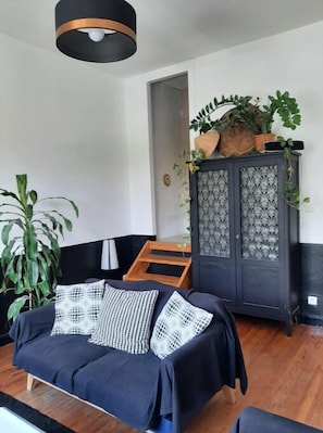 Un salon comprenant un canapé, un meuble avec des panneaux de verre décoratifs et un luminaire suspendu.