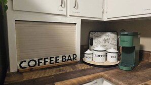 Eine Küchenarbeitsplatte mit einer Kaffeebar-Beschilderung, einer Keurig-Kaffeemaschine und Behältern mit den Aufschriften 'Zucker', 'Kaffee' und 'Tee'.