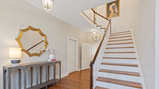 A staircase with wooden steps and a white railing, a console table with a lamp, a mirror, and a vase with flowers. - Experience the heart of downtown, where historic charm meets modern comforts. (Huntsville)