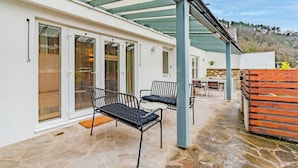 A covered patio area with stone flooring, two black metal chairs, and a table. - The Weir House - Symonds Yat (Symonds Yat)