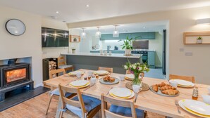 A modern kitchen with a central island, a dining area with wooden furniture, and a fireplace. - The Weir House - Symonds Yat (Symonds Yat)