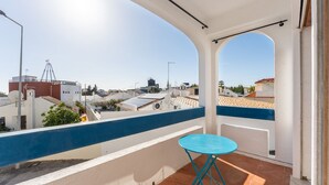 Ein Balkon mit blauem Tisch, weißen Wänden und Blick auf die Stadt.