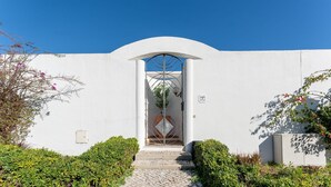 A white building with a central arched doorway, a small garden with hedges, and a clear blue sky. - Cozy 2 BDR W/Balcony in Vale do Lobo by LovelyStay (Almansil)