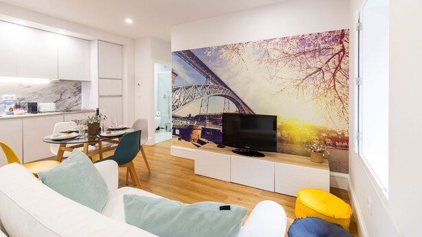 Ett modernt vardagsrum med en soffa, ett matbord för två personer, en tv och en stor väggmålning som föreställer Eiffeltornet.