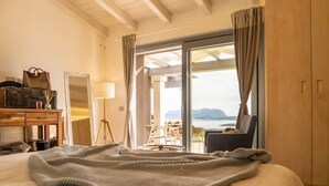 A hotel room with a bed, a desk with a lamp, a chair, and a view of the sea through a sliding door. - Pittulongu Olbia Residence A Domo Mea Retreat (Pittulongu)