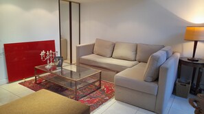 Ett modernt vardagsrum med ett soffbord i glas, en beige soffa, en röd accentvägg och en mönstrad matta.