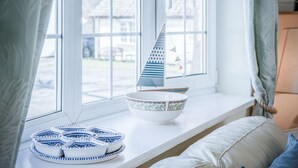 Ein Fenster mit einem Segelbootsmodell, einer dekorativen Schale und einem Teller-Set in Blau und Weiß auf einem weißen Regal.