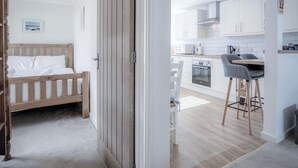 Ein modernes Schlafzimmer mit einem Holzbett, einer Küchenzeile mit weißen Schränken und einer Essecke mit einem Barhocker.
