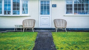 Ein Gebäude mit weißer Fassade, einer schwarzen Tür und zwei Korbstühlen davor.
