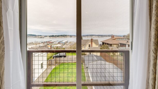 A view from a window with a grid pattern, overlooking a residential area with houses, a road, and a body of water. - Port Orchard Guest House - Walk to Bay Street! (Port Orchard)