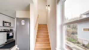 A modern kitchen with a built-in microwave, oven, and refrigerator. A wooden staircase leads to a landing with a view of the backyard. - Port Orchard Guest House - Walk to Bay Street! (Port Orchard)