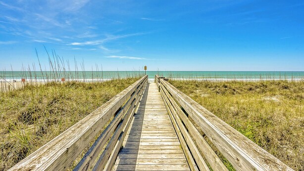 Een houten looppad dat naar een strand leidt, onder heldere luchten.