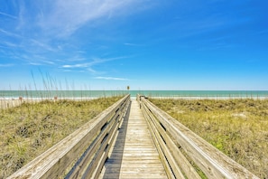A wooden boardwalk leading to a beach with clear skies.