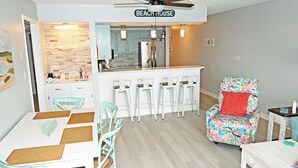 Een keuken met een bar, een eettafel met stoelen en een kleurrijke fauteuil.